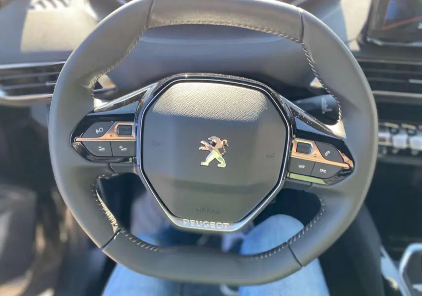 Gros plan sur le volant compact multifonctions noir du Peugeot 5008 avec logo lion chromé au centre.