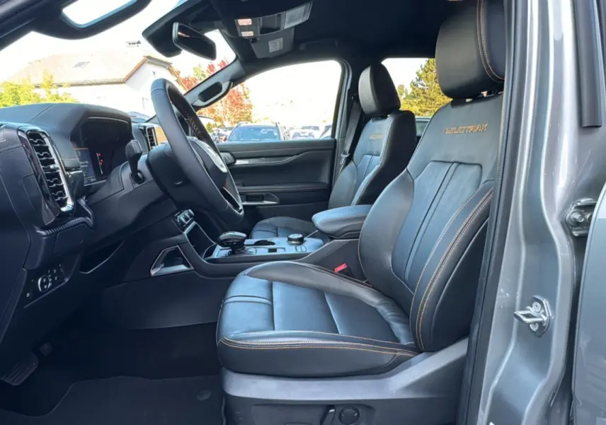Vue intérieure côté conducteur du Ford Ranger 2.3 PHEV Wildtrak Plus 2025 avec sièges cuir noirs et surpiqûres orange.