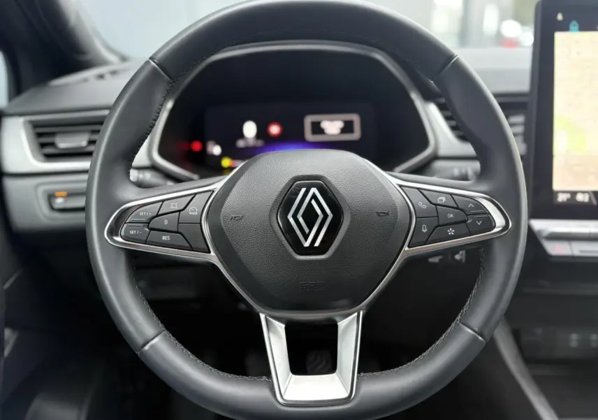 Gros plan sur le volant noir du Renault Captur TCE 100 Techno 2025 avec commandes intégrées et tableau de bord numérique flou.