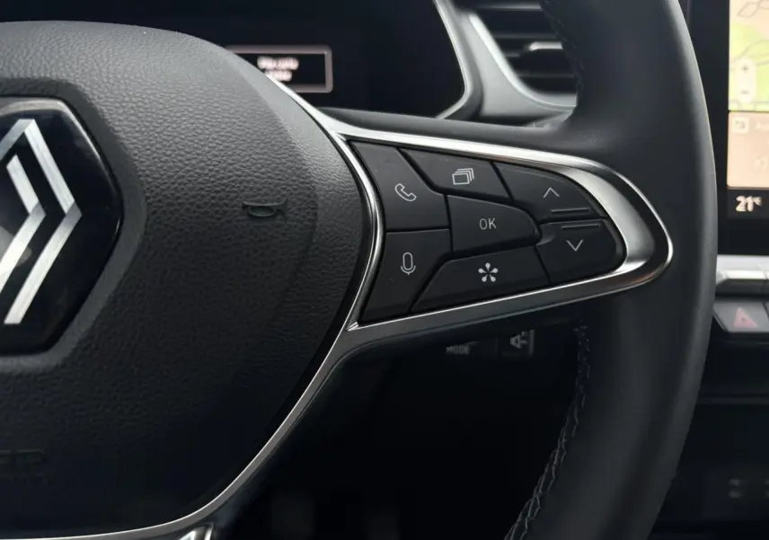 Gros plan sur le volant du Renault Captur TCE 100 Techno 2025, avec commandes intégrées et logo Renault visible.