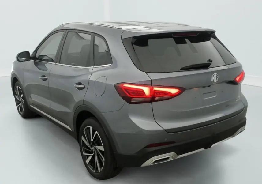 Vue 3/4 arrière gauche de la MG3 1.5 L HYBRID+ 195 CH Luxury en blanc Dover avec feux arrière allumés et jantes noires.