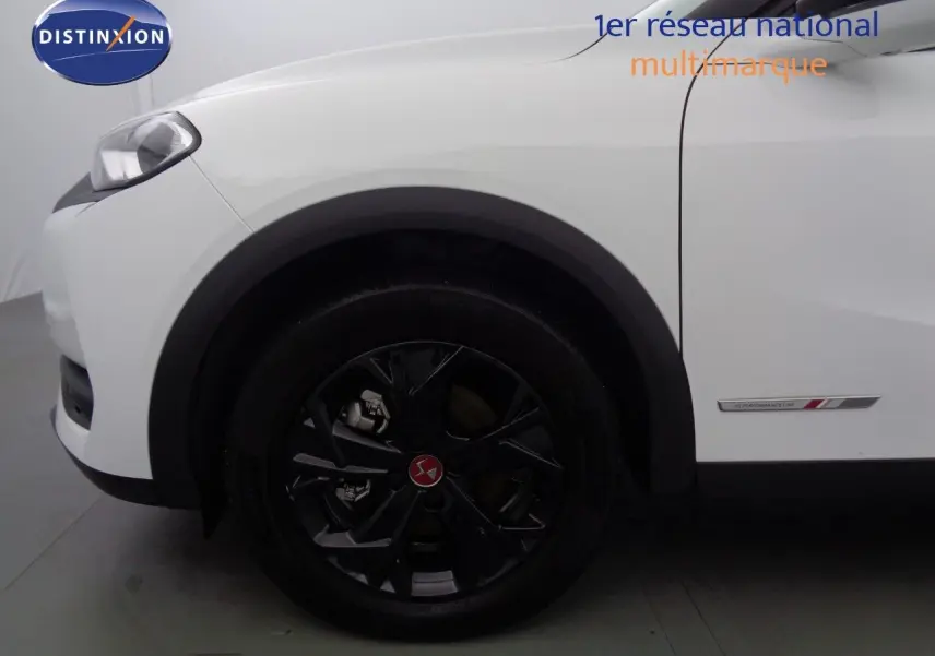 Gros plan sur la roue avant gauche noire et la carrosserie blanche banquise du DS3 Crossback 1.5 BlueHDi 130 Performance Line.