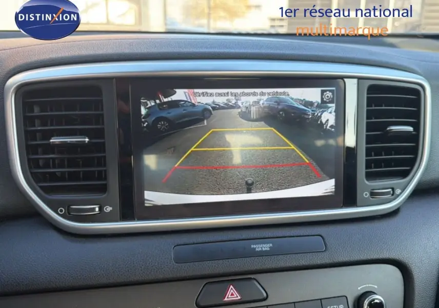 Vue intérieure du tableau de bord du Kia Sportage blanc nacré, affichant la caméra de recul sur l'écran central.