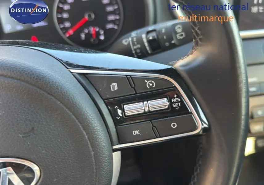 Gros plan sur les commandes au volant en cuir noir du Kia Sportage blanc nacré, avec tableau de bord en arrière-plan flou.