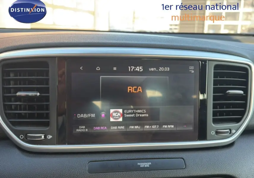 Écran tactile central du tableau de bord du Kia Sportage blanc nacré, affichant la radio RCA en mode DAB/FM.