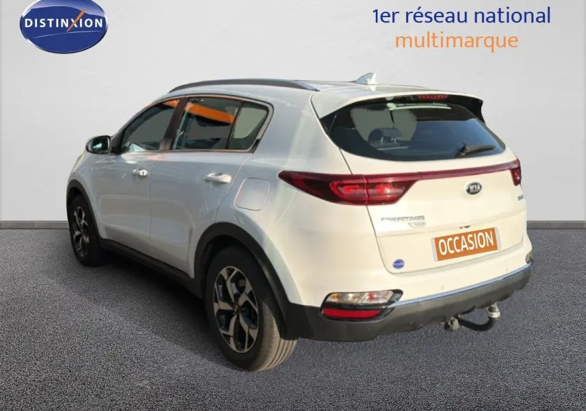 Vue 3/4 arrière droite d'un Kia Sportage blanc nacré avec attelage et jantes bi-ton.