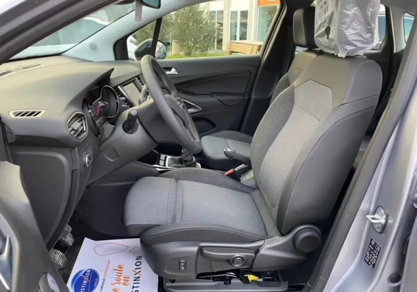 Vue intérieure côté conducteur de l'Opel Crossland gris alu 2022, montrant siège tissu et tableau de bord moderne.