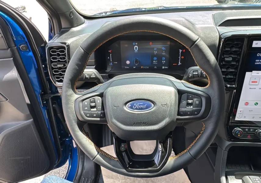 Vue intérieure centrée sur le volant cuir noir avec surpiqûres orange du Ford Ranger Bleu Lightning 2026.
