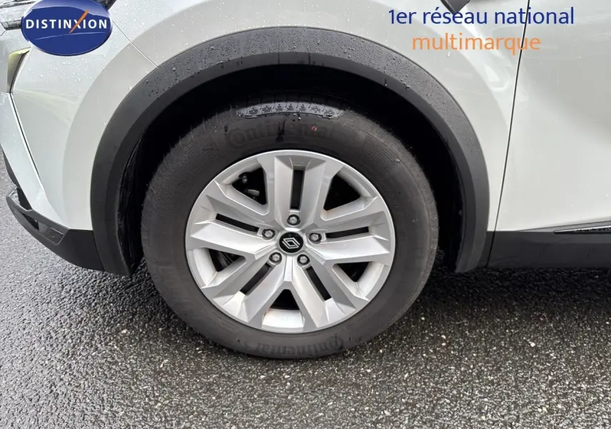 Gros plan sur la roue avant gauche d’un Renault Symbioz blanc nacré, avec jante alliage et logo central visible.