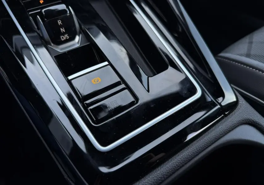 Gros plan sur la console centrale noire brillante avec levier de vitesse automatique et frein de stationnement électrique d’une Volkswagen Golf VIII.