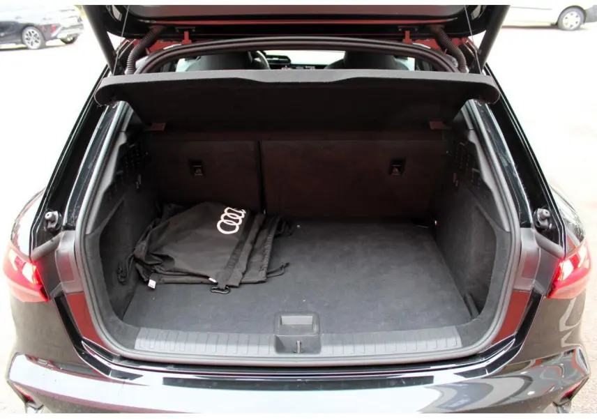 Coffre ouvert vu de l'arrière d'une Audi A3 Sportback noir Mito Metal avec sac Audi à l'intérieur.