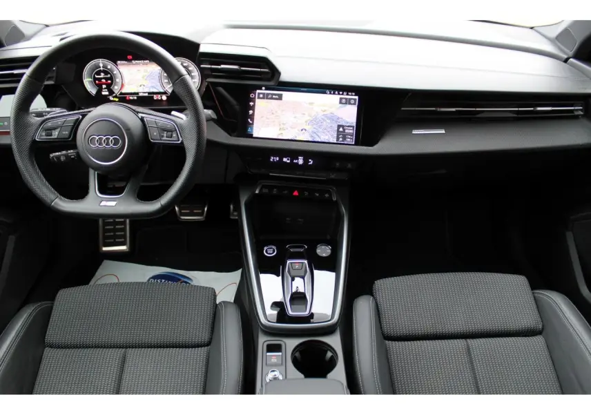 Vue intérieure avant de l'Audi A3 Sportback 2025, tableau de bord noir avec écran tactile et volant cuir multifonctions.