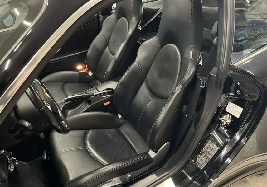Vue intérieure côté conducteur d'une Porsche 911 Targa 997 Carrera 4S noire avec sièges sport en cuir noir et accoudoir central.