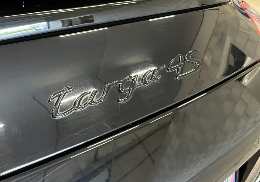 Gros plan sur l’inscription Targa 4S en chrome sur la partie arrière noire métallisée d’une Porsche 911.