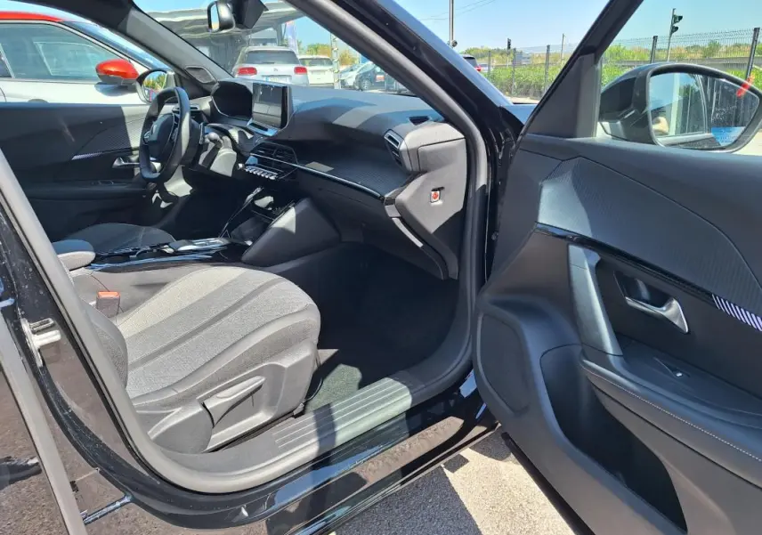 Intérieur avant droit du Peugeot 2008 Hybrid noir 2025, montrant siège tissu, tableau de bord et écran tactile.