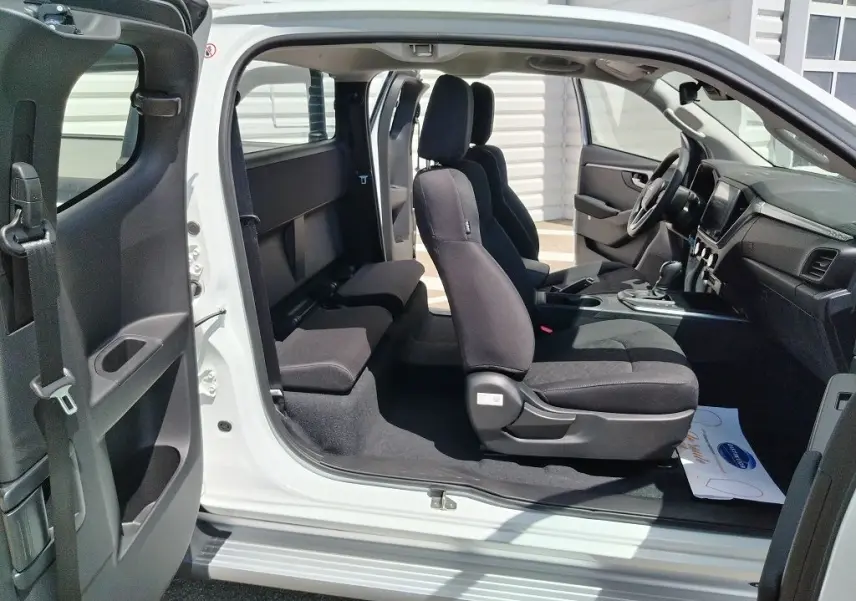 Vue latérale intérieure du pick-up Isuzu D-MAX blanc 2026, montrant les sièges avant et arrière en tissu noir.