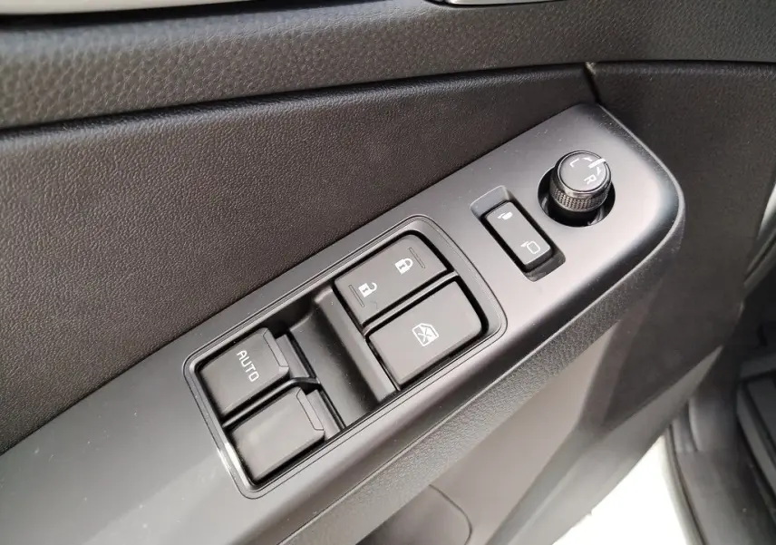 Gros plan sur les commandes de lève-vitres et réglage des rétroviseurs côté conducteur d'un Isuzu D-MAX blanc.