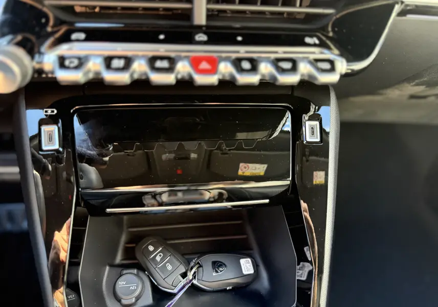Gros plan intérieur sur la console centrale noire brillante du Peugeot 2008 Hybrid 145 GT avec clé posée dans le rangement.