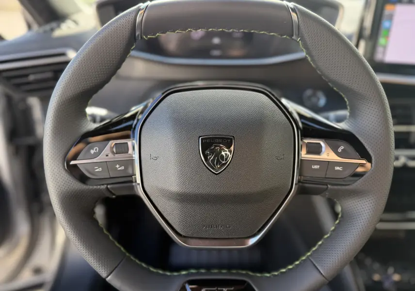 Gros plan sur le volant cuir perforé noir avec surpiqûres vertes du Peugeot 2008 Hybrid 145 GT, logo lion central visible.