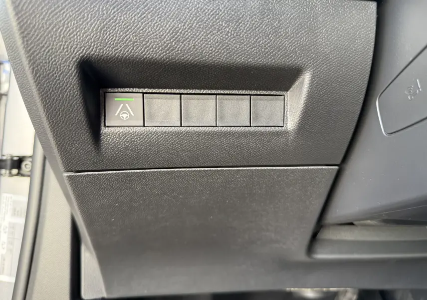 Bouton d'assistance au maintien de voie avec témoin vert sur la partie inférieure gauche du tableau de bord noir du Peugeot 2008 Hybrid 145 GT.
