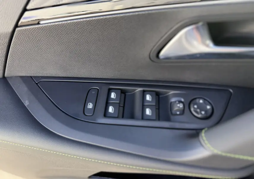 Détail des commandes de lève-vitres et réglages des rétroviseurs sur la porte côté conducteur d’un Peugeot 2008 gris Artense toit noir.