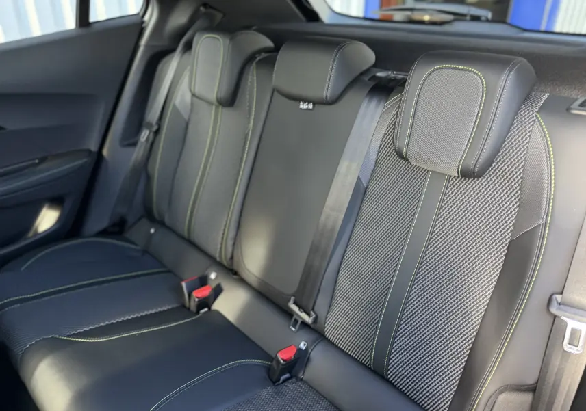 Vue intérieure sur les sièges arrière du Peugeot 2008 Hybrid 145 gris, avec surpiqûres vertes et ceintures noires.