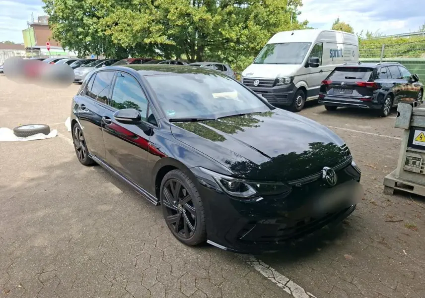 Volkswagen Golf 8 R-Line noire vue 3/4 avant avec jantes noires et attelage escamotable visible.