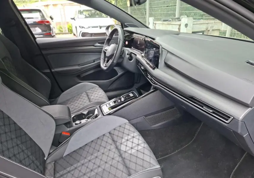 Vue intérieure côté conducteur de la Volkswagen Golf 8 R-Line 2024, avec sièges sport en tissu gris à motifs et tableau de bord moderne.