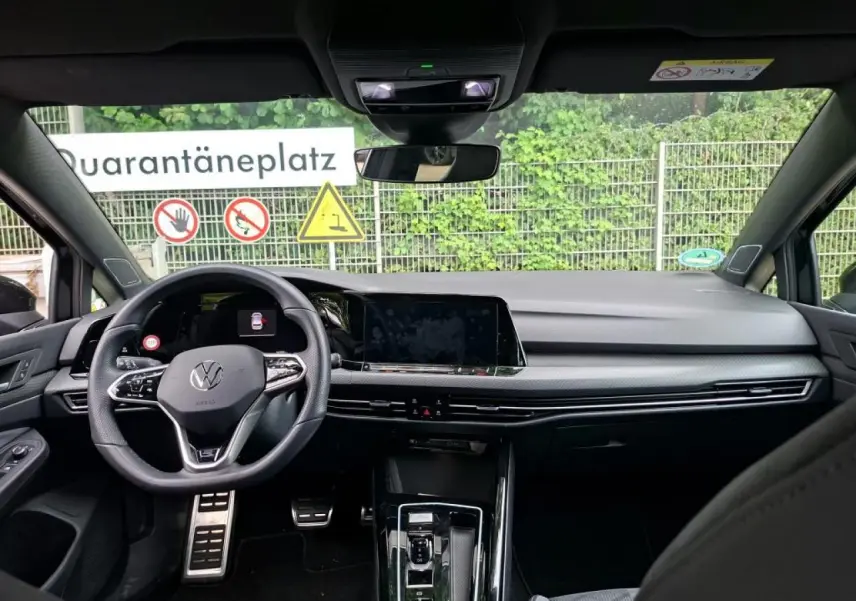 Vue intérieure avant de la Volkswagen Golf 8 noire, mettant en valeur le volant multifonction et l'écran tactile central.