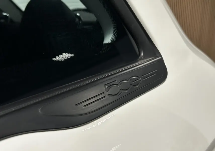 Gros plan sur l'emblème noir 500e sur la portière côté droit d'une FIAT 500 électrique blanche.