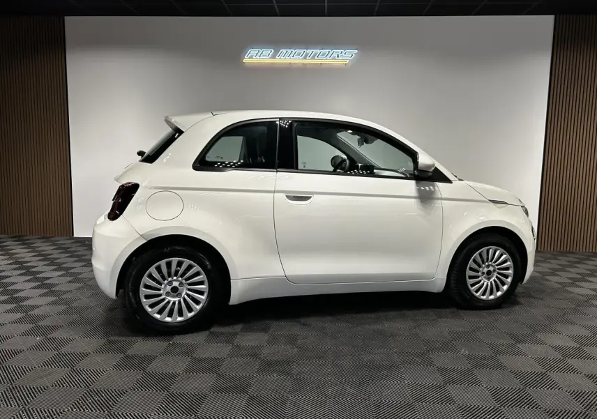 Profil droit d'une Fiat 500 électrique blanche 2024, avec jantes alliage et intérieur visible à travers les vitres.