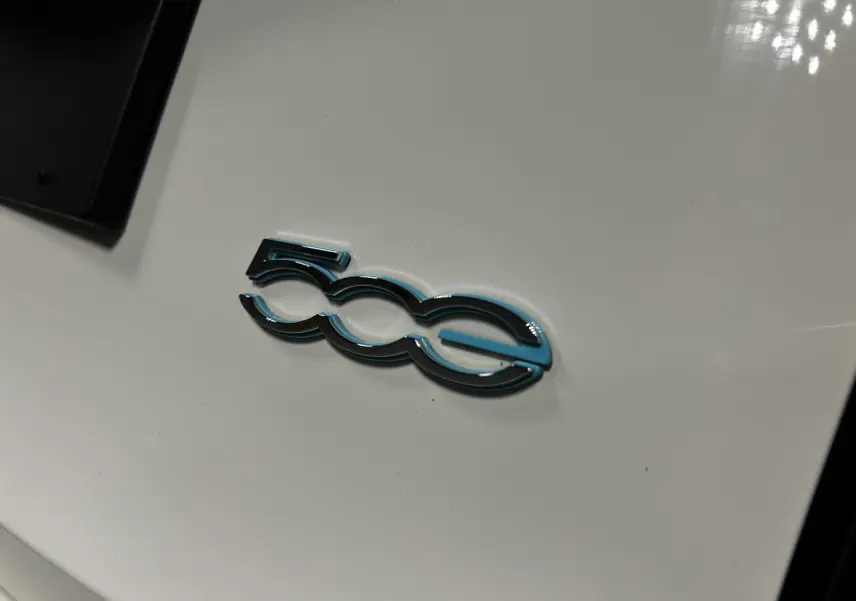 Gros plan sur l'emblème "500e" bleu et noir sur la carrosserie blanche d'une Fiat 500 électrique 2024.