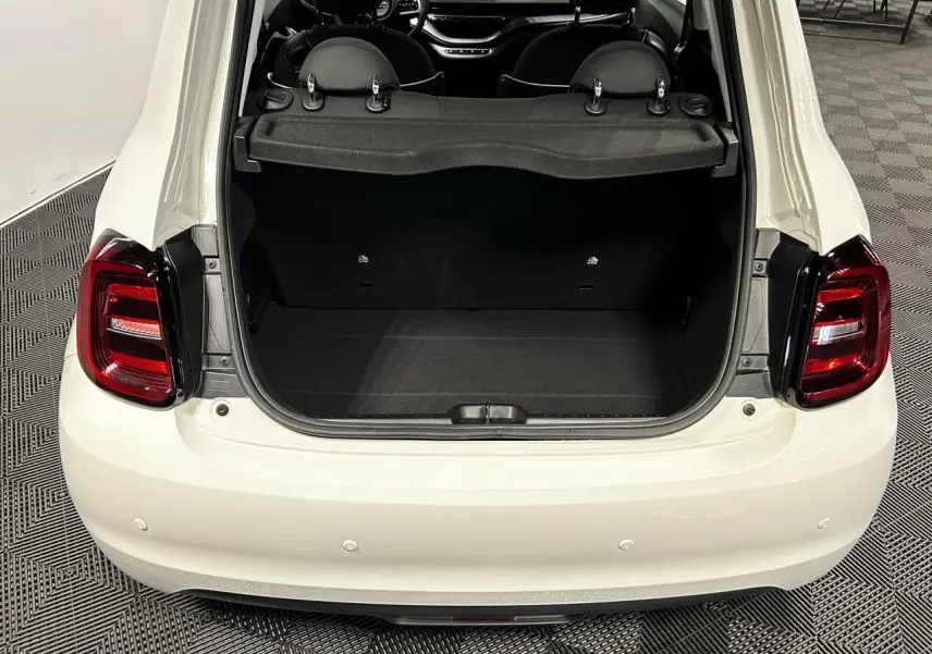 Vue arrière ouverte du coffre d'une FIAT 500 électrique blanche 2024, avec intérieur noir et feux arrière LED rouges.