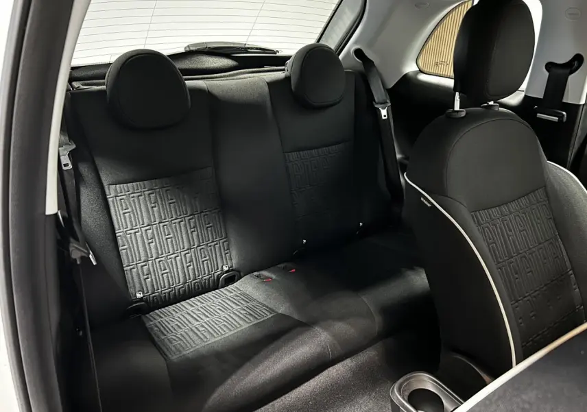 Vue intérieure arrière de la Fiat 500 2024 électrique, sièges tissu noir avec monogramme FIAT et appuie-têtes ronds.