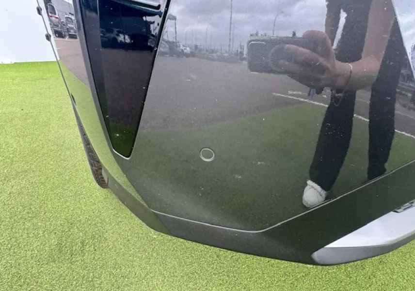 Gros plan sur le pare-chocs avant gris titane du Peugeot 3008 II avec capteur de stationnement visible.