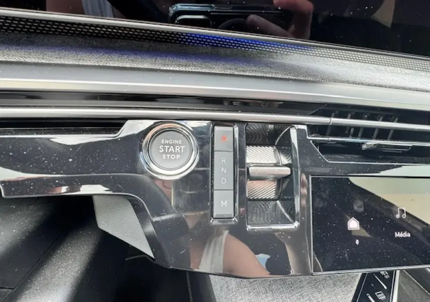 Gros plan sur la console centrale noire brillante du Peugeot 3008 II hybride 2024, avec bouton start/stop et sélecteur de vitesses.