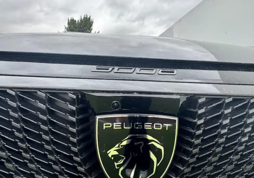 Gros plan sur la calandre noire et le logo lion du Peugeot 3008 gris titane, détail du lettrage 3008 sur le capot.