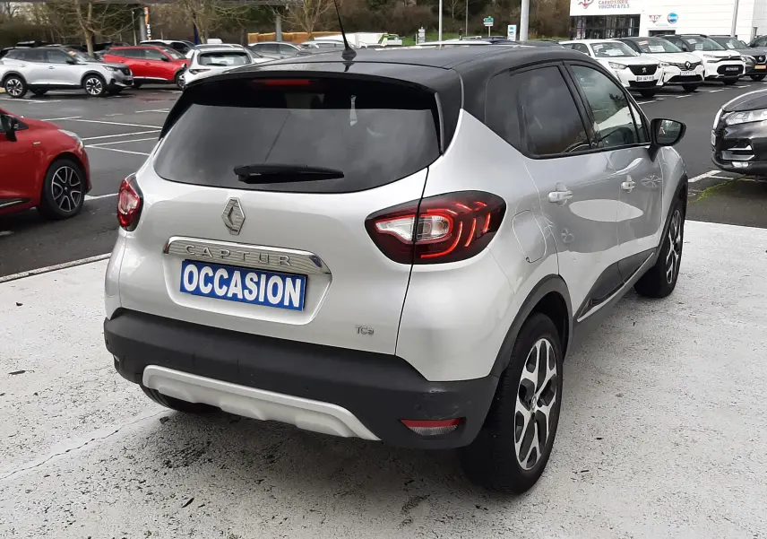 Vue 3/4 arrière droite d'un Renault Captur gris avec toit noir, feux arrière allumés, sur parking extérieur.