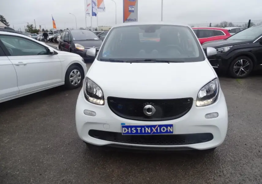 Vue avant d'une Smart Forfour Electric Drive Prime blanche avec calandre noir brillant et feux allumés sur parking.
