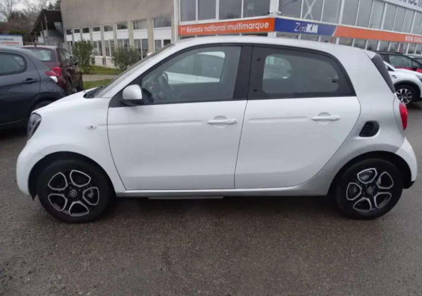 Vue latérale gauche d'une Smart Forfour électrique blanche avec jantes alliage bicolores et toit gris clair.