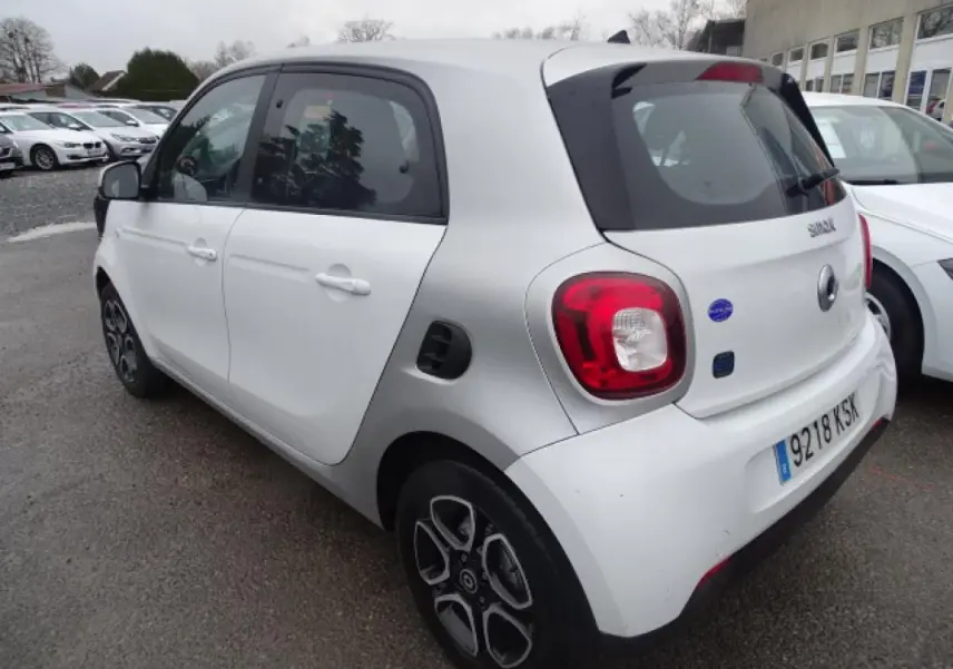 Vue 3/4 arrière droite d'une Smart Forfour électrique blanche avec jantes alliage bicolores et logo EQ sur le hayon.