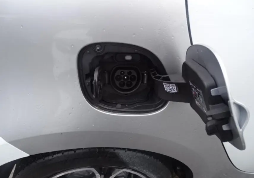 Gros plan sur la prise de recharge côté gauche d’une Smart Forfour électrique blanche, avec port ouvert au-dessus de la roue arrière.