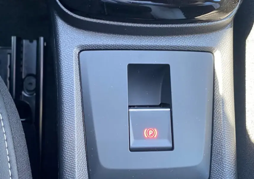 Gros plan sur le bouton de frein de stationnement électrique au centre de la console d'une Citroën C3 Aircross gris Mercury.