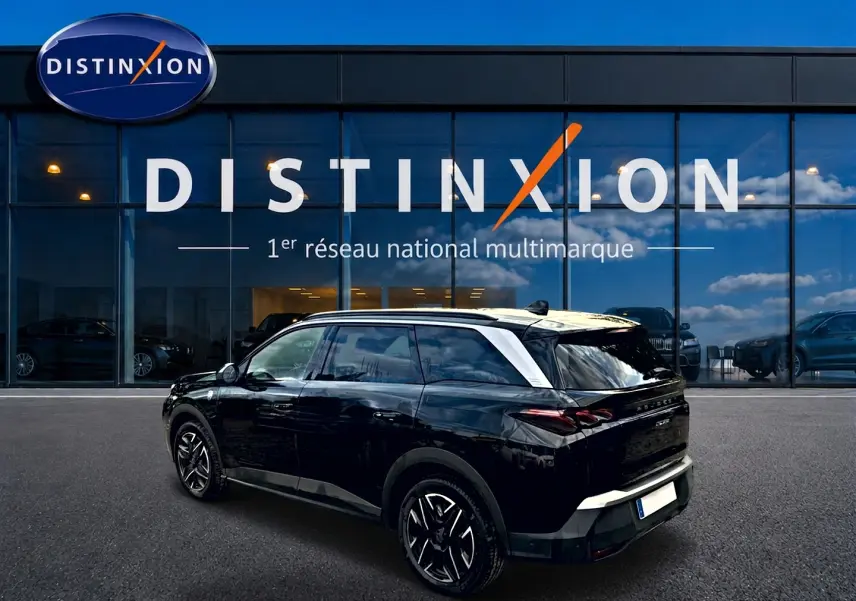Vue 3/4 arrière droite d'un Peugeot 5008 Hybrid 145 GT noir avec toit contrasté blanc devant un showroom Distinxion.