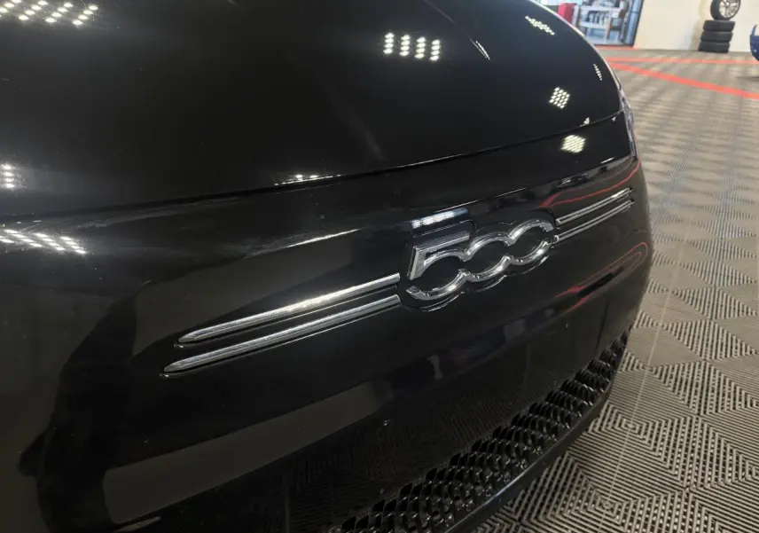 Gros plan sur l’avant noir brillant d’une FIAT 500 électrique 2024 avec logo 500 chromé et calandre inférieure ajourée.