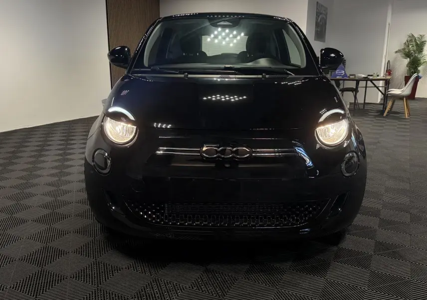 Vue de face d'une FIAT 500 électrique noire avec phares allumés dans un intérieur showroom.