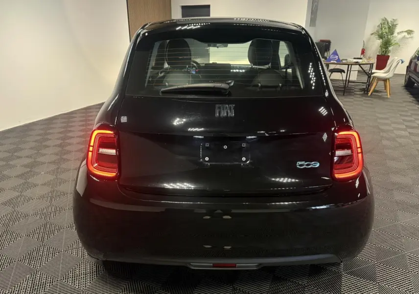 Vue arrière d'une Fiat 500 électrique noire 2024 avec feux arrière allumés dans un showroom.