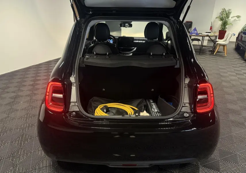 Vue arrière ouverte de la Fiat 500 électrique noire 2024, coffre visible avec câble de recharge jaune à l'intérieur.