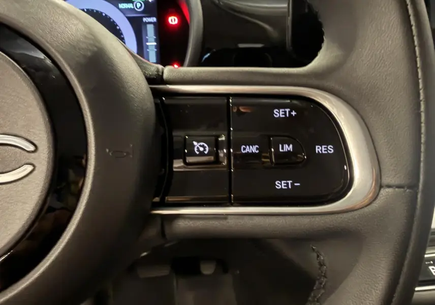 Gros plan sur les commandes du régulateur de vitesse du volant noir soft-touch d'une Fiat 500 électrique 2024.