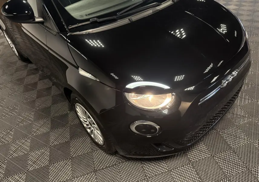 Vue 3/4 avant droit d'une Fiat 500 électrique noire avec phare avant allumé et jantes acier 15 pouces.
